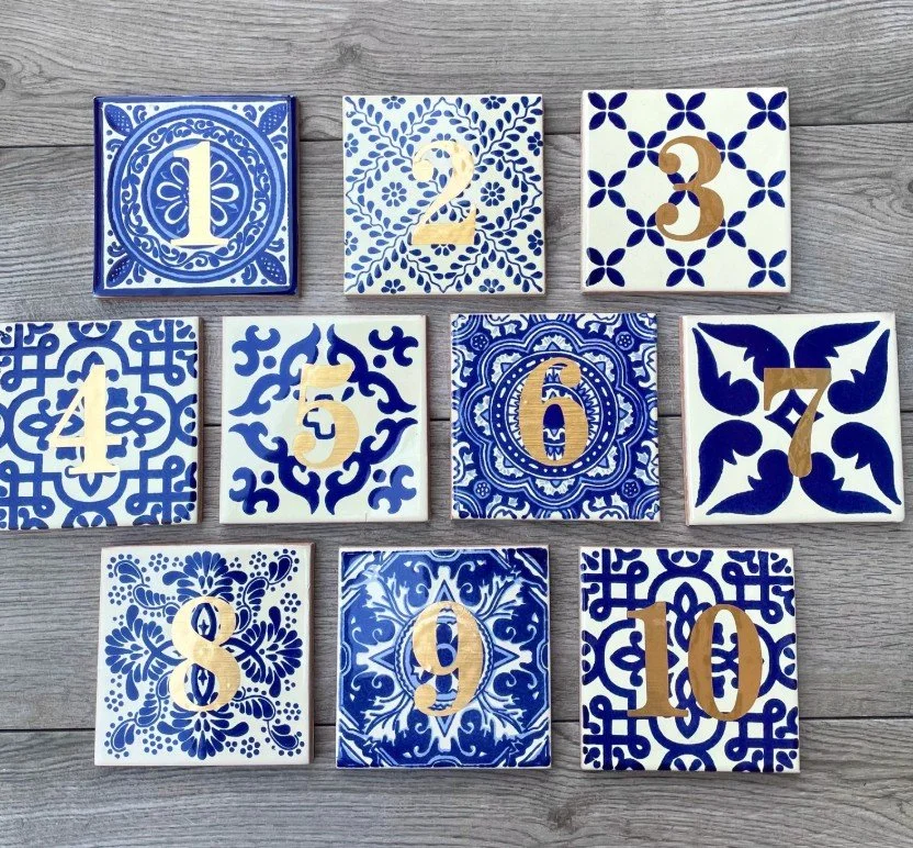 Eine Anordnung von zehn quadratischen Keramikfliesen mit verschiedenen blau-weißen Mustern und mittig platzierten goldenen Ziffern von 1 bis 10.