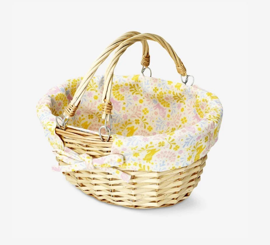 Kleiner geflochtener Weidenkorb von Flying Tiger mit zwei Henkeln und einem Stoff-Innenfutter mit buntem Blumen- und Hasenmuster sowie einer Schleife.