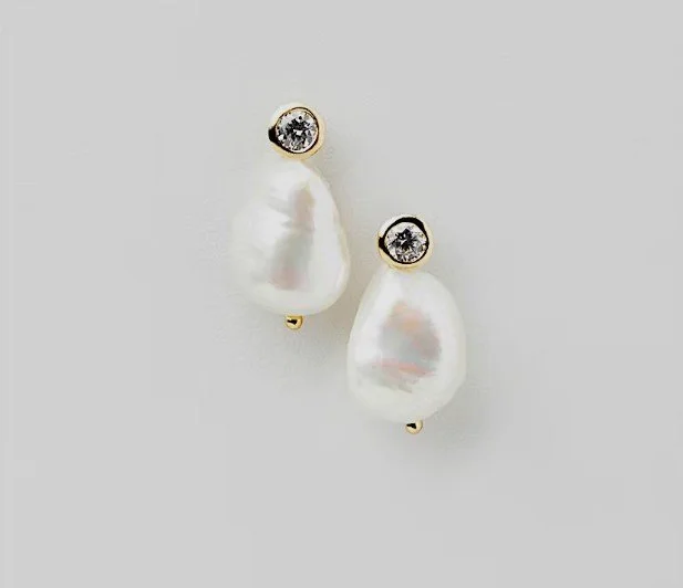 Goldene Ohrstecker mit rundem Zirkonia-Kristall und anhängender weißer Barock-Perle (organische Form). Eleganter, moderner Brautschmuck von Safira, ideal als trendige Brautohrringe.