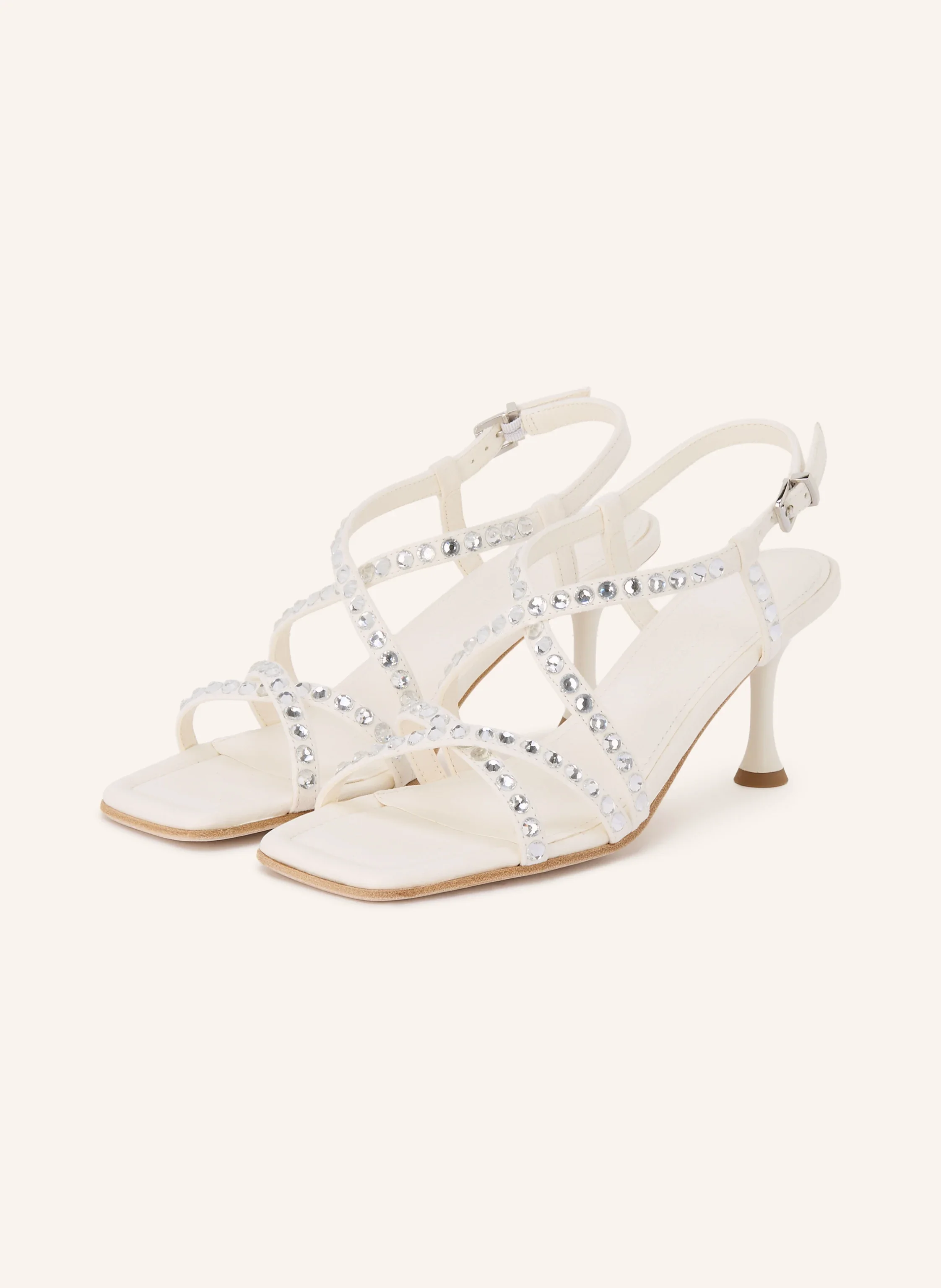 Weiße Riemchensandalen mit eckiger Zehenpartie, glitzerndem Kristallbesatz auf den Riemen und mittelhohem Pfennigabsatz vor hellem Hintergrund.