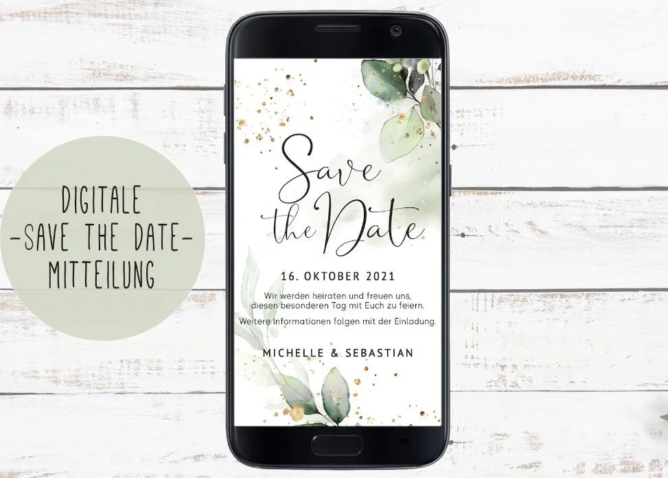 Smartphone auf weißem Holz. Vertikale digitale Save‑the‑Date-Karte mit Eukalyptus und goldenen Glitzerpunkten. Text: 16. Oktober 2021, Michelle & Sebastian. Links runder salbeigrüner Sticker: „Digitale Save the Date‑Mitteilung“.