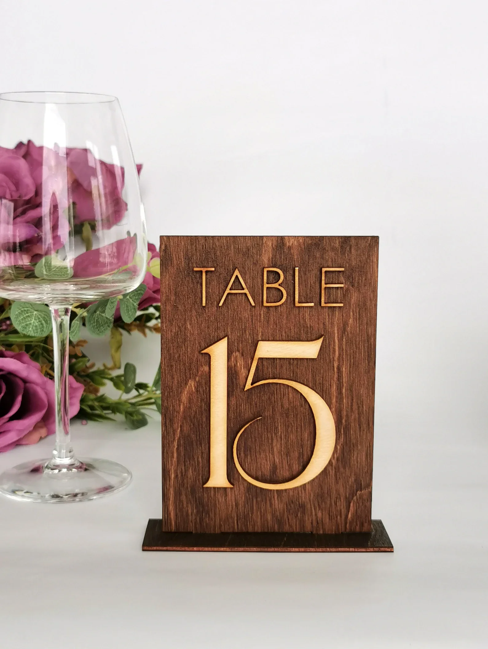 Eine dunkle Echtholzplatte in einem passenden Ständer mit der eingravierten oder aufgesetzten hellen Aufschrift „TABLE 15“.