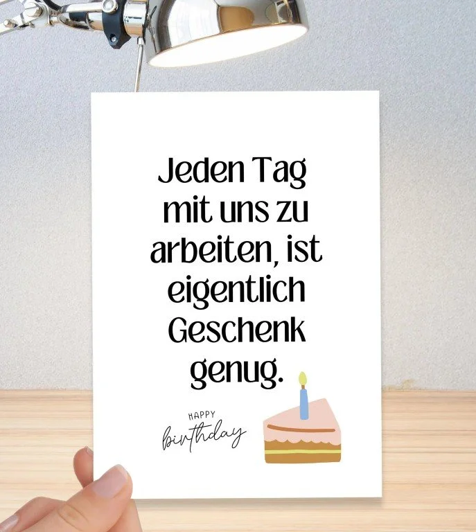 Witzige Geburtstagskarte mit dem Spruch: „Jeden Tag mit uns zu arbeiten, ist eigentlich Geschenk genug.“ Darunter ein Stück Kuchen mit Kerze und der Text „Happy Birthday“.