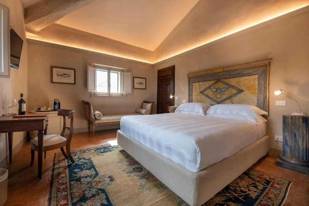 Foto eines eleganten Schlafzimmers mit beigen Wänden, indirekter Deckenbeleuchtung und einem großen Bett mit kunstvoll verziertem Kopfteil auf einem Orientteppich.