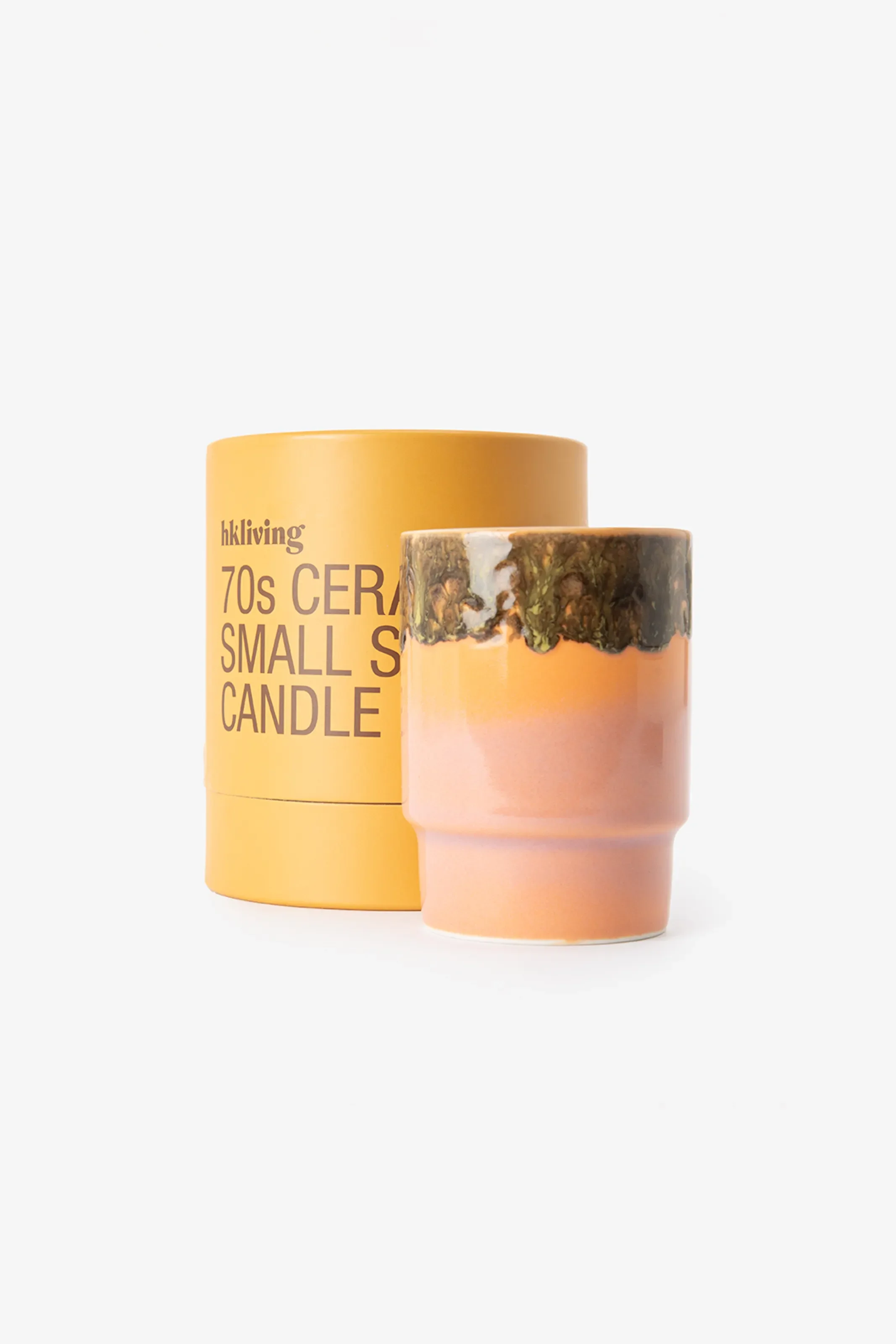Keramik-Kerze im 70er-Look von hkliving. Der Becher ist pfirsich-orange mit dunkelgrün-braunem Glasurrand. Daneben die gelbe Zylinder-Verpackung mit Aufschrift.