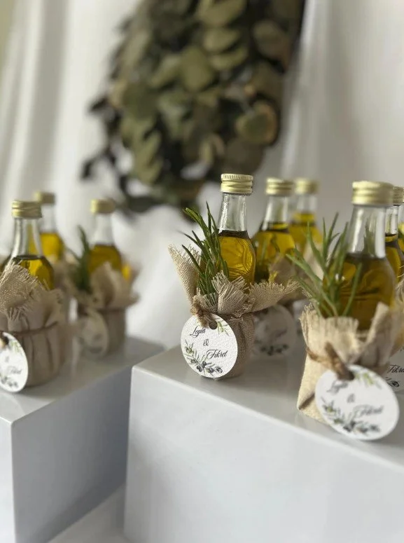 Kleine Flaschen Olivenöl als Hochzeitsgastgeschenke, liebevoll dekoriert mit Jutestoff, Rosmarinzweigen und personalisierten Anhängern.
