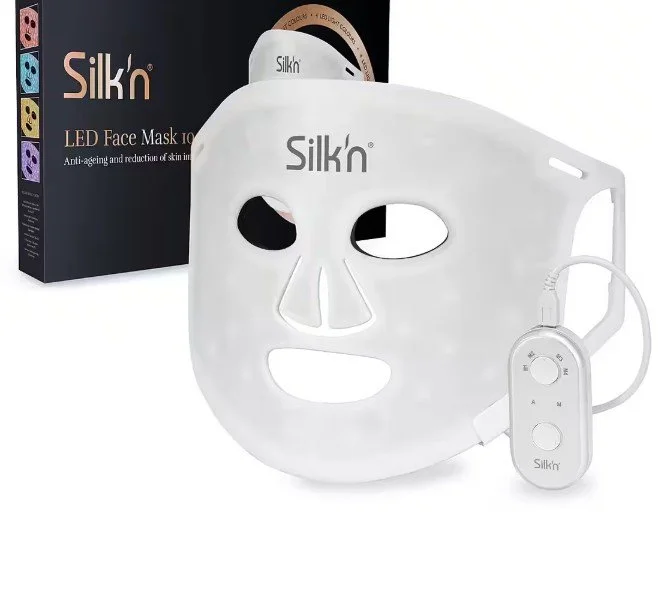 Silk'n LED Face Maske zur Lichttherapie für zu Hause. Die weiße Gesichtsmaske ist zusammen mit dem kabelgebundenen Steuergerät und der Originalverpackung abgebildet.