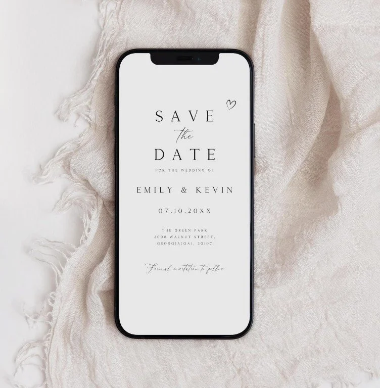 Schwarzes Smartphone auf hellem Leinenstoff. Display: minimalistische Save‑the‑Date‑Karte in Schwarz auf Weiß für Emily & Kevin.