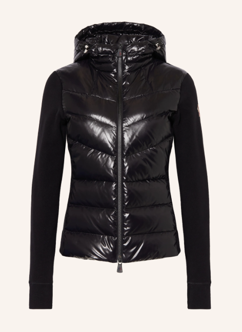 Eine schwarze, figurbetonte Skijacke mit Kapuze und durchgehendem Frontreißverschluss. Das Design zeichnet sich durch einen Materialmix aus einer hochglänzenden, gesteppten Rumpfpartie und matten, glatten Ärmeln aus.