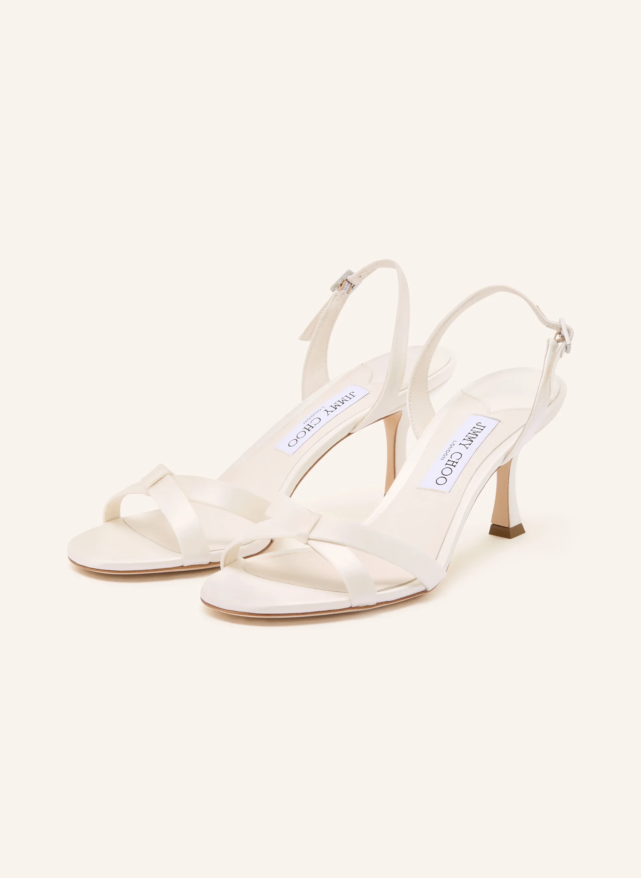 Cremeweiße Satin-Sandalen von Jimmy Choo mit gekreuzten Riemen, schmalem Fersenriemchen und mittelhohem Stiletto-Absatz vor hellem Hintergrund.