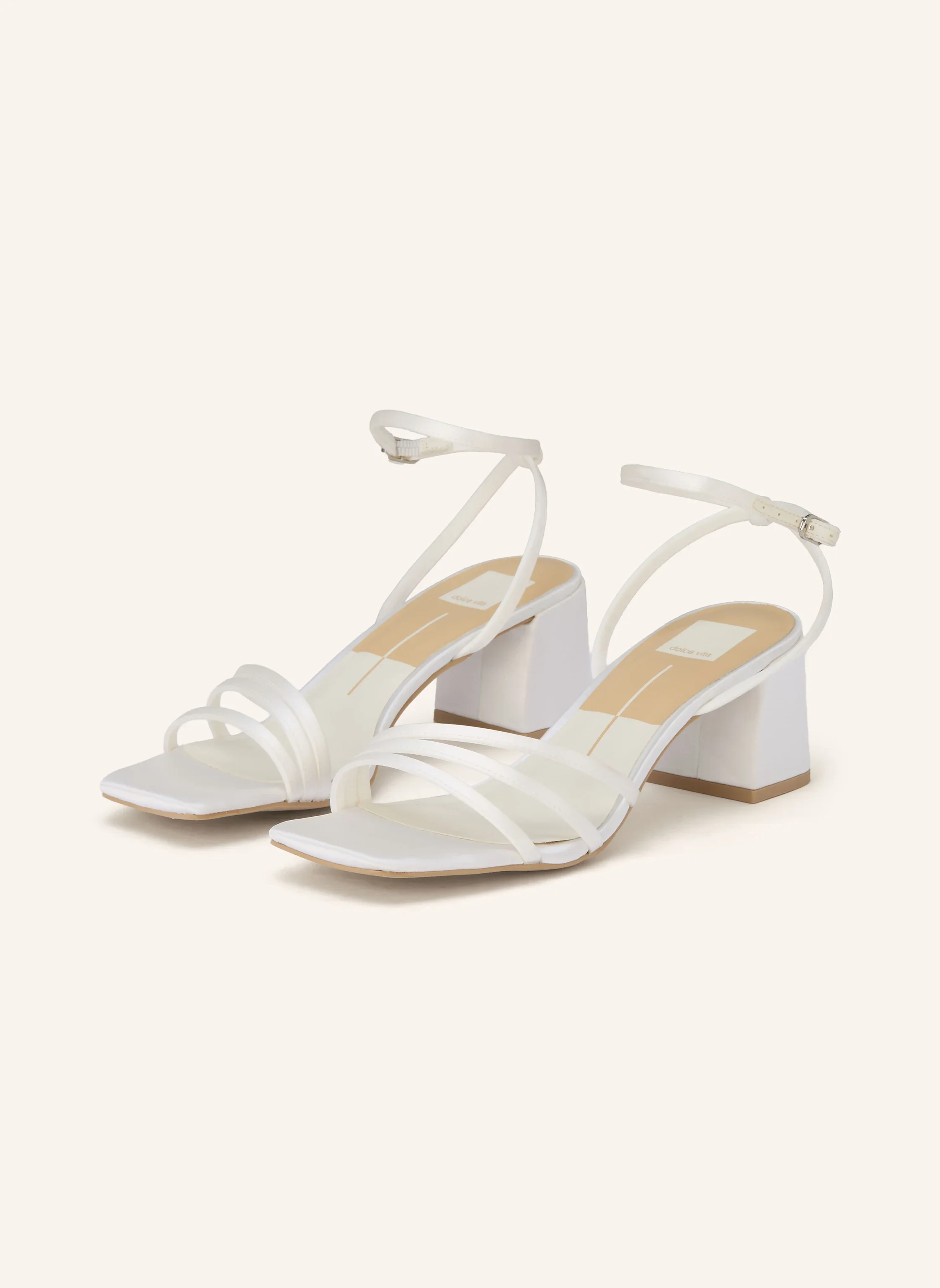 Weiße Riemchensandalen von Dolce Vita mit eckiger Zehenpartie und Blockabsatz vor hellem Hintergrund.