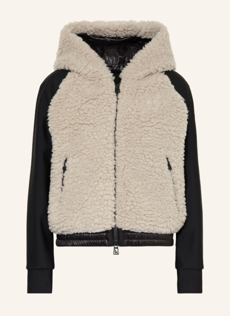 Eine Jacke mit beigefarbenem Teddyfell an Rumpf und Kapuze, abgesetzt mit glatten schwarzen Ärmeln, einem schwarzen Saum und Frontreißverschluss.