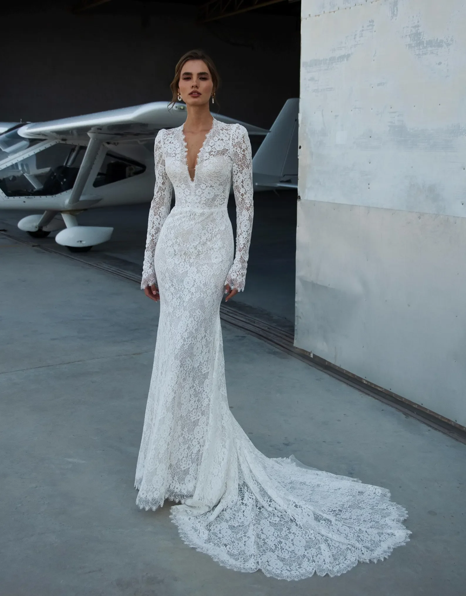 Braut in eng anliegendem Spitzen-Brautkleid mit tiefen V-Ausschnitt, langen Spitzenärmeln und elegantem Schleppe – handgefertigtes Meerjungfrau-Brautkleid von Alma de Luz Atelier