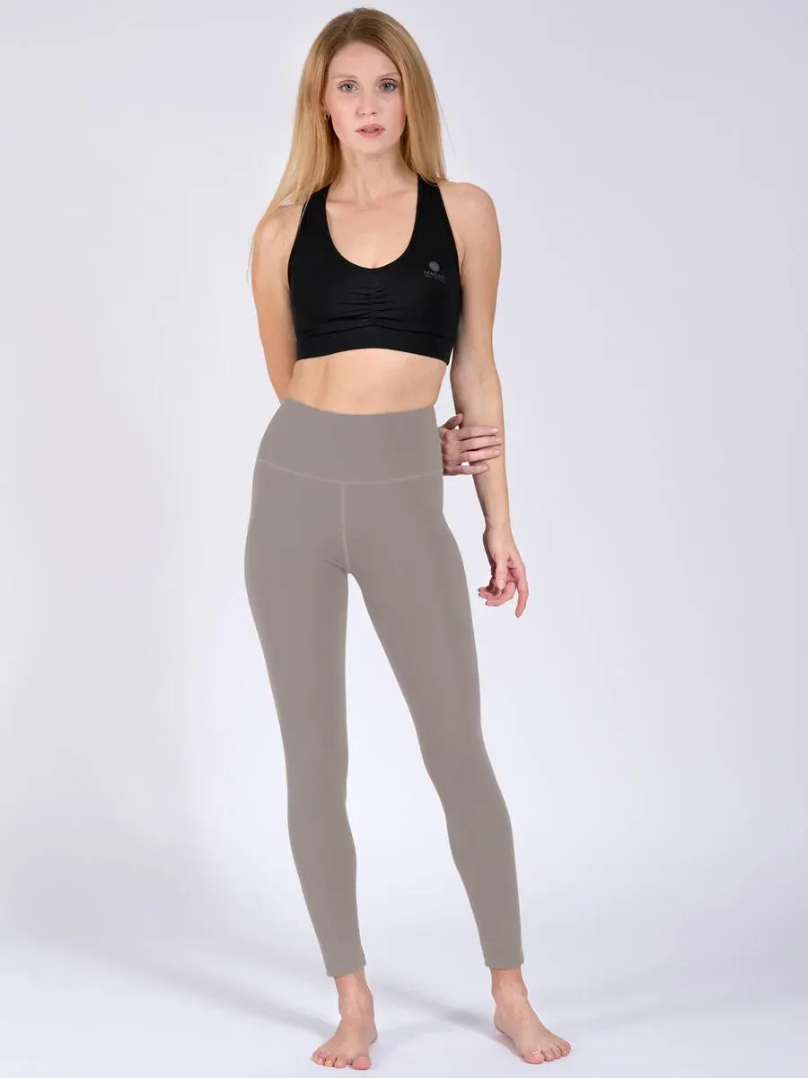Frau in schwarzem Sport-BH und taupefarbenen Leggings vor hellem Hintergrund