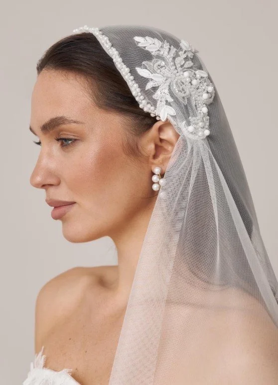 Nahaufnahme einer Braut im Profil mit einem edlen Tüllschleier, der am Haaransatz mit Perlenbordüren und floralen 3D-Spitzenapplikationen verziert ist. Hochwertige Brautmode-Inspiration für den Brautschleier-Guide im Holistic Mag.