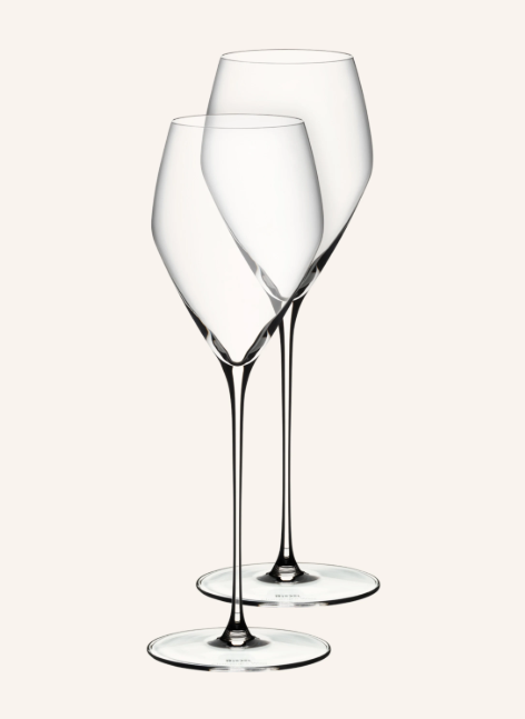 Zwei elegante, leere Weingläser von Riedel. Sie stehen leicht versetzt hintereinander und haben extrem lange, feine Stiele sowie einen markanten, eckig geformten Kelch aus Klarglas.