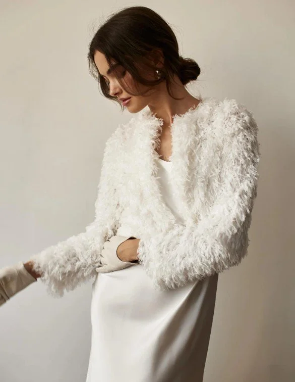 Braut trägt eine elegante, flauschige weiße Brautjacke im Bolero-Stil über einem schlichten Satinkleid – stilvoller Look für die Winterhochzeit.