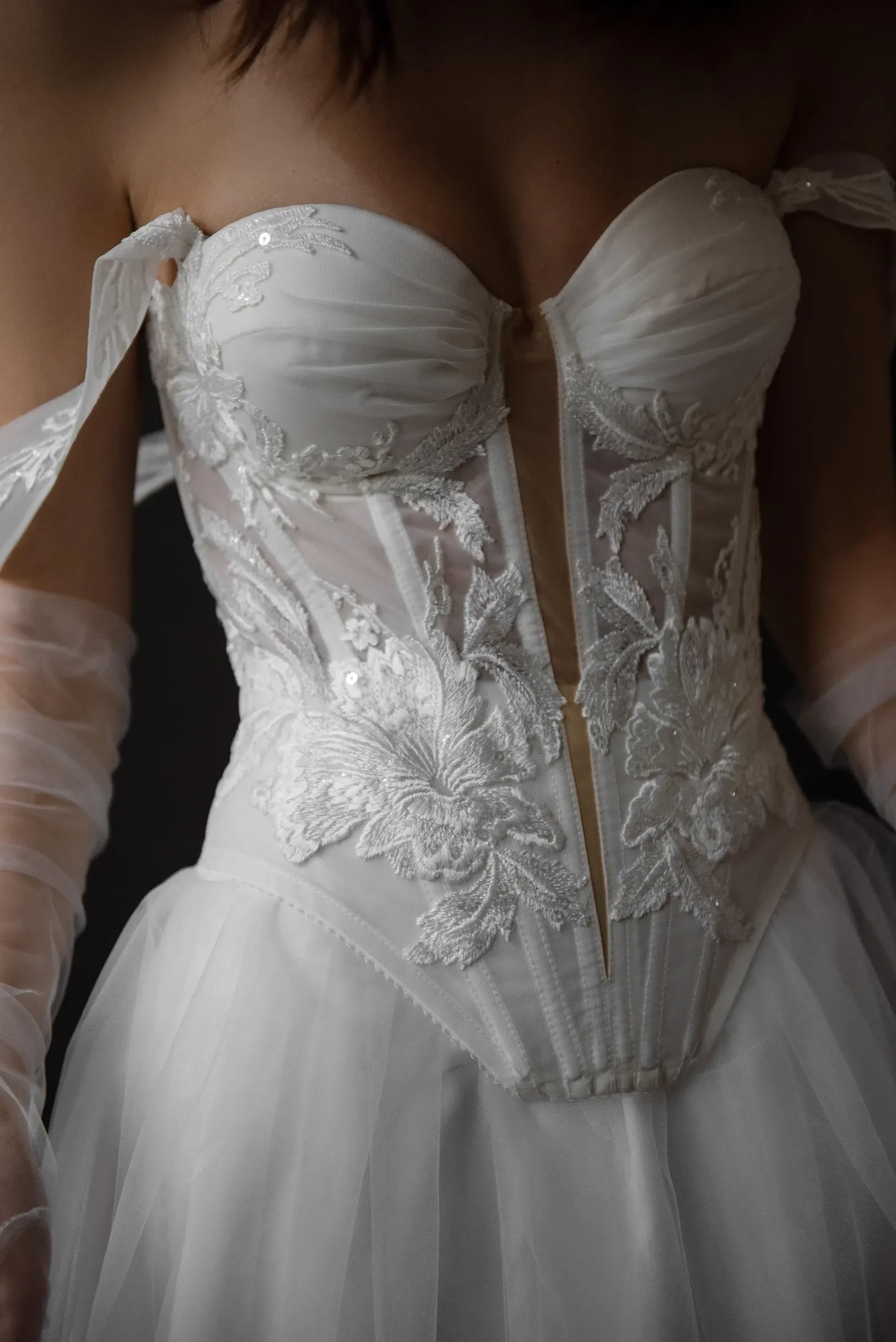 Detailaufnahme eines modernen Brautkleid-Korsetts mit kunstvoller floraler Spitze, halbtransparenten Details und zarten Off-Shoulder-Ärmeln aus Tüll.
