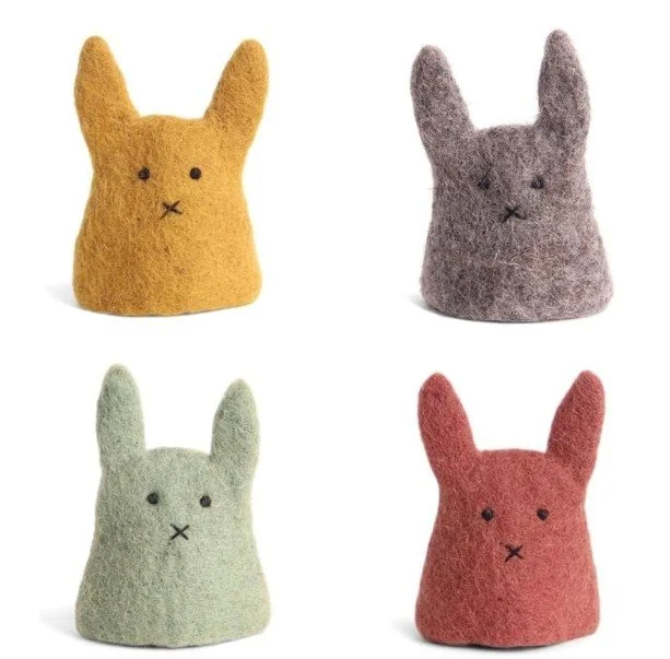 Vier minimalistische Eierwärmer aus Filz in Hasen-Form (Gelb, Grau, Salbei, Terrakotta) vor weißem Hintergrund.