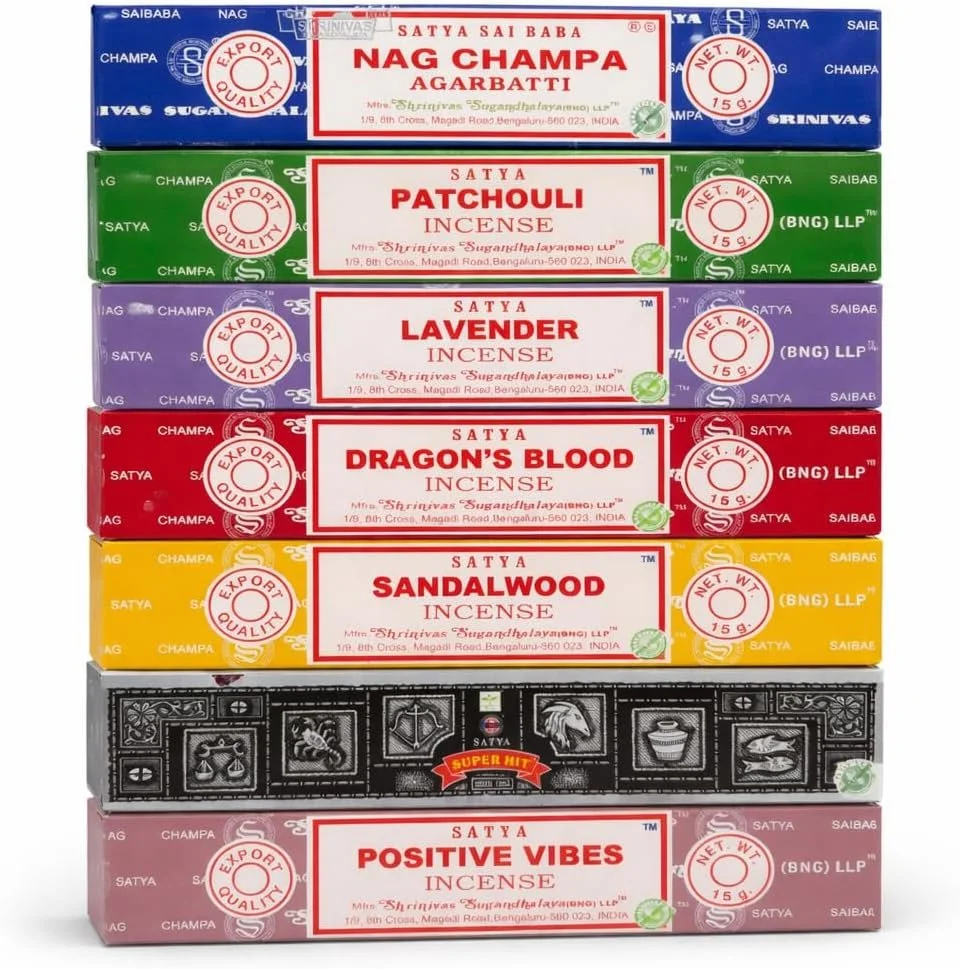 Stapel aus sieben verschiedenfarbigen Räucherstäbchen-Verpackungen der Marke Satya. Es sind von oben nach unten folgende Sorten zu sehen: Nag Champa, Patchouli, Lavender, Dragon's Blood, Sandalwood, Super Hit und Positive Vibes.