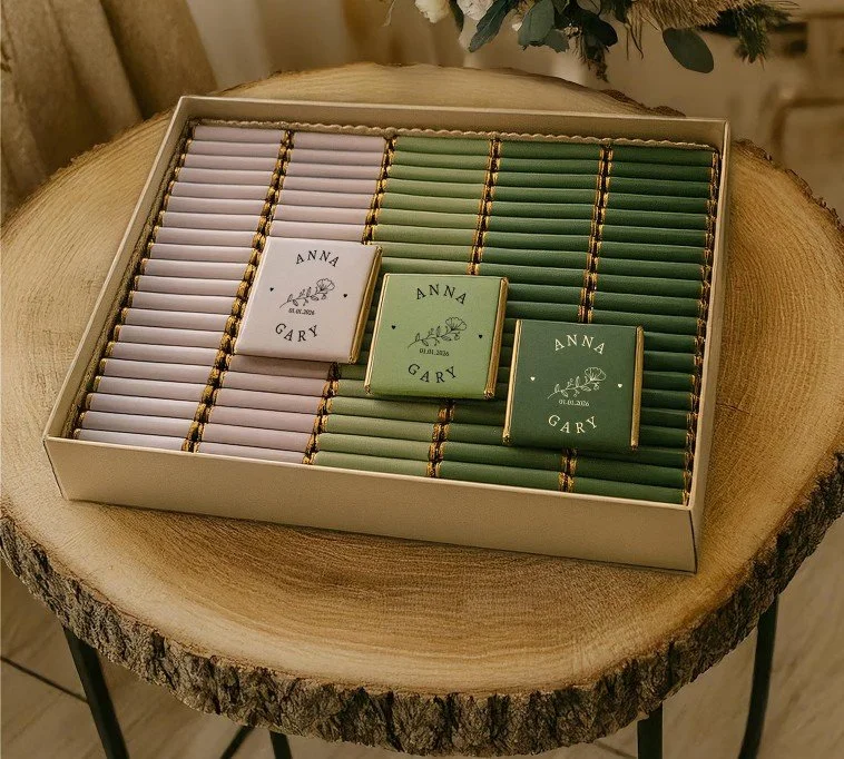 Personalisierte Schokoladen-Gastgeschenke zur Hochzeit in Flieder und Grün. Die Täfelchen sind mit den Namen „Anna & Gary“ und dem Datum 2026 bedruckt.