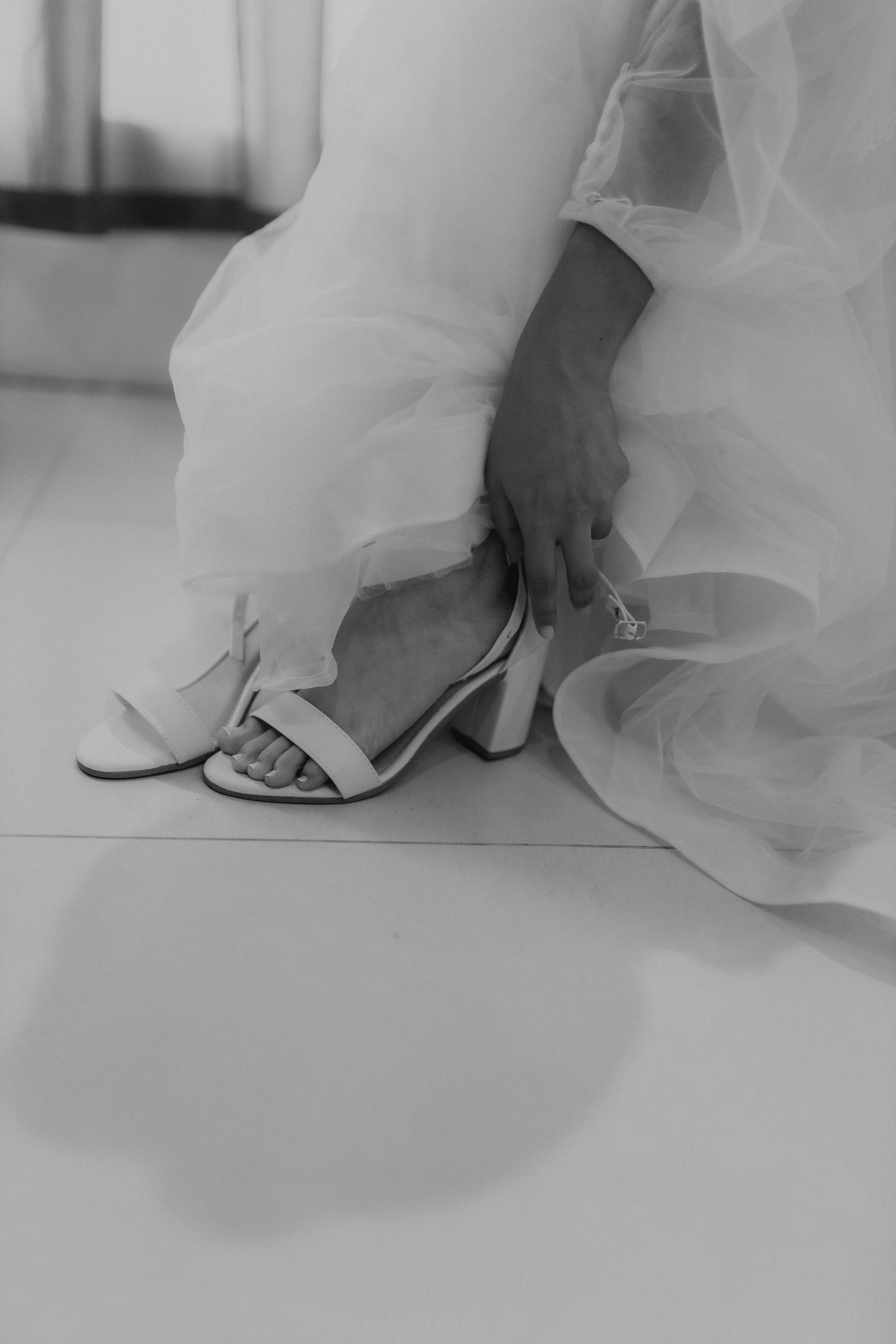 Elegante weiße Brautschuhe mit Blockabsatz als Riemchen-Sandale, getragen zu einem fließenden weißen Hochzeitskleid.