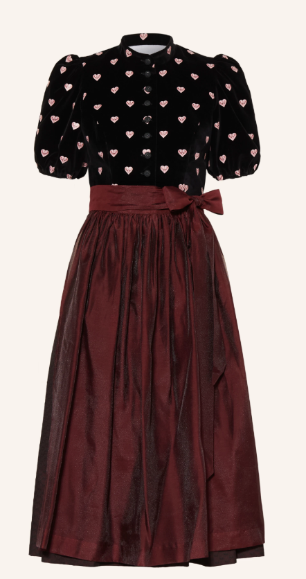 Dirndl mit schwarzem Samtmieder, rosa Herzchenmuster, Puffärmeln und Stehkragen, kombiniert mit weinrotem, glänzendem Taftrock und passender Schleife an der Taille.