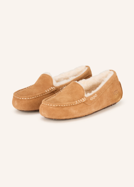 Ein Paar hellbraune UGG Hausschuhe aus Wildleder im Mokassin-Stil. Sie haben helle Ziernähte und sind innen mit dicker, flauschiger weißer Wolle gefüttert.
