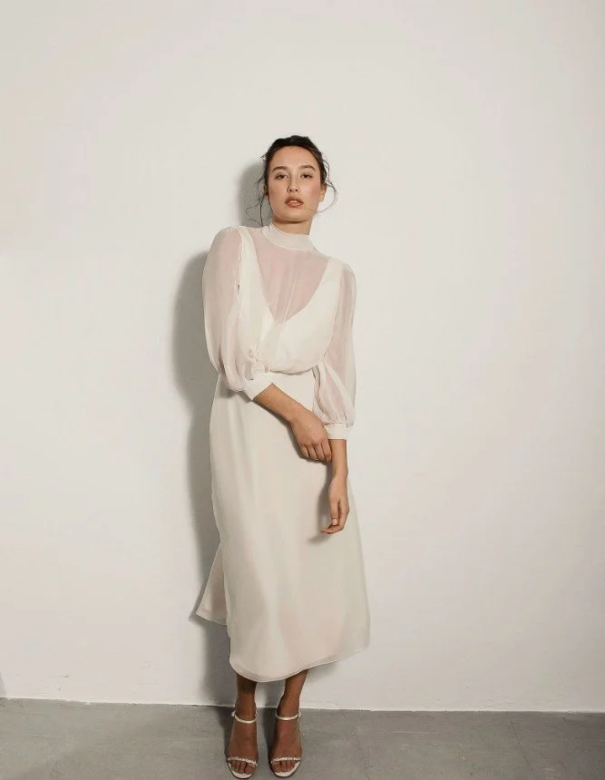 Modernes Midi-Brautkleid im Lagen-Look mit transparentem Organza-Oberteil und langen Ärmeln.