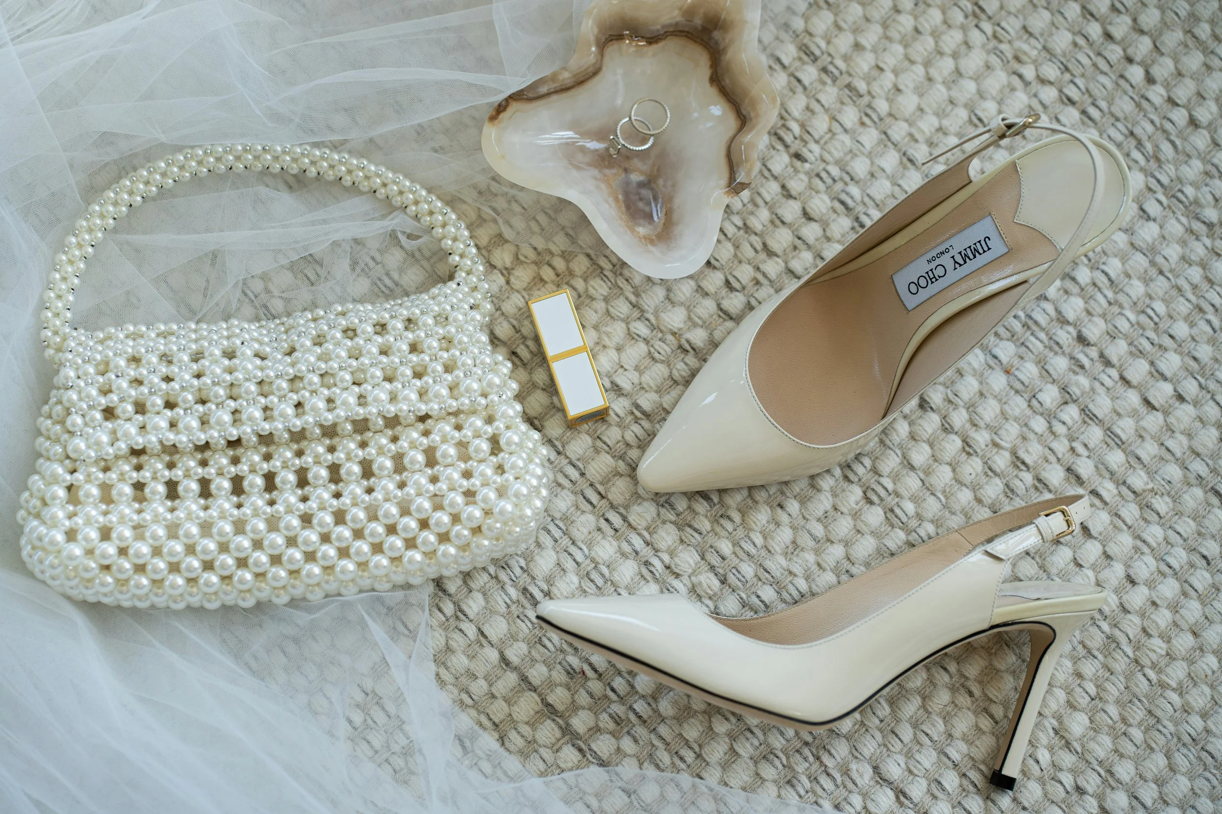 Perlenkette, Ringe, Parfüm, High Heel Schuhe, und eine Tasche auf einem Teppichboden