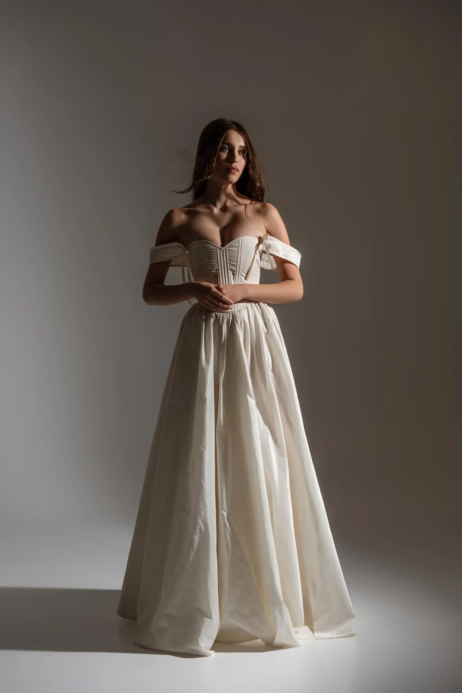 Ganzkörperaufnahme eines modernen, eleganten Brautkleides mit strukturiertem Korsett-Oberteil, romantischen schulterfreien Ärmeln und einem voluminösen, fließenden Rock.