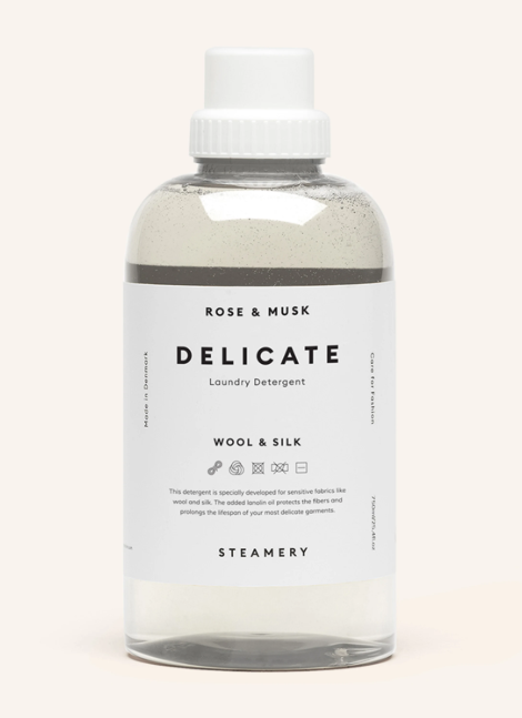 transparente Flasche mit weißer Verschlusskappe, die mit Flüssigwaschmittel gefüllt ist. Auf dem weißen Etikett steht der Markenname „STEAMERY“ und in schwarzer Schrift darunter „DELICATE Laundry Detergent“