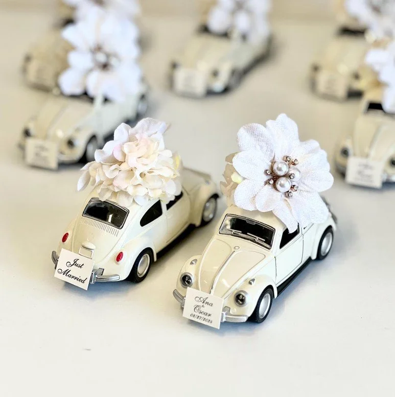 Miniatur-Oldtimer als Hochzeitsgastgeschenke, geschmückt mit weißen Blumen und kleinen „Just Married“-Schildern, liebevoll arrangiert.