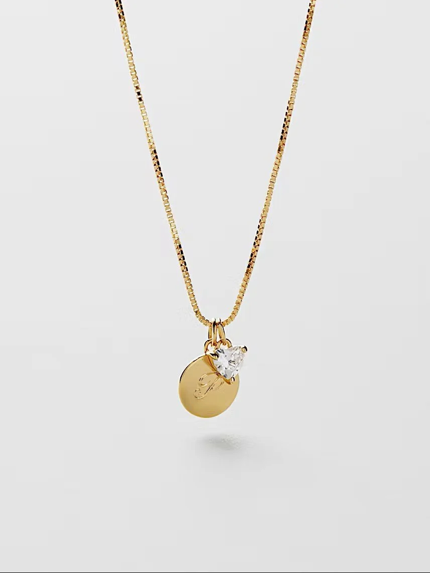 Eine feine goldene Kette. Als Anhänger dienen ein rundes, glattes Goldplättchen (Gravur "P") und ein kleiner, herzförmiger Glitzerstein.