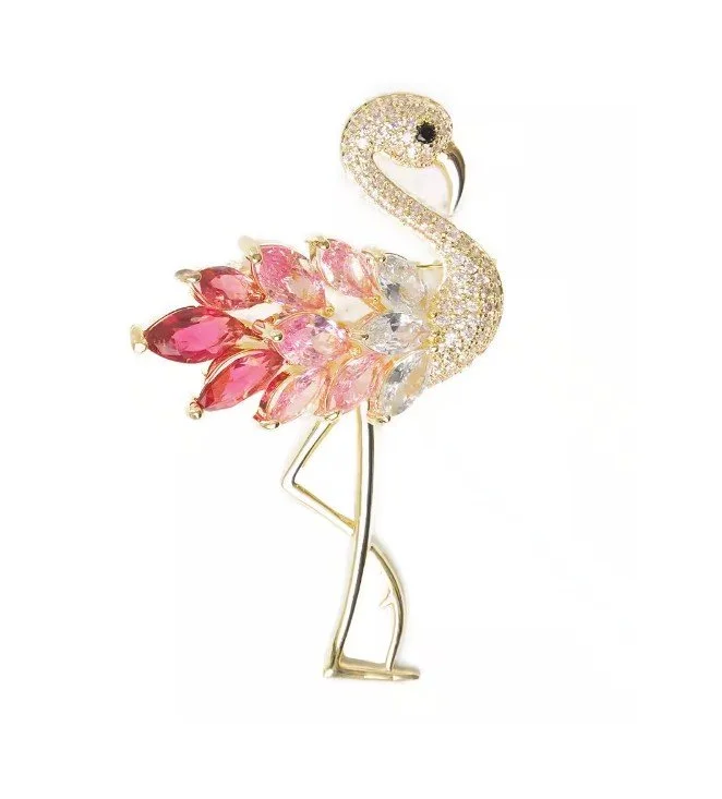 Goldfarbene Flamingo-Brosche auf weißem Grund. Körper mit pinken und rosafarbenen Kristallen, Hals und Kopf mit weißen Kristallen besetzt. Hochwertiger Schmuck für den Sommer.
