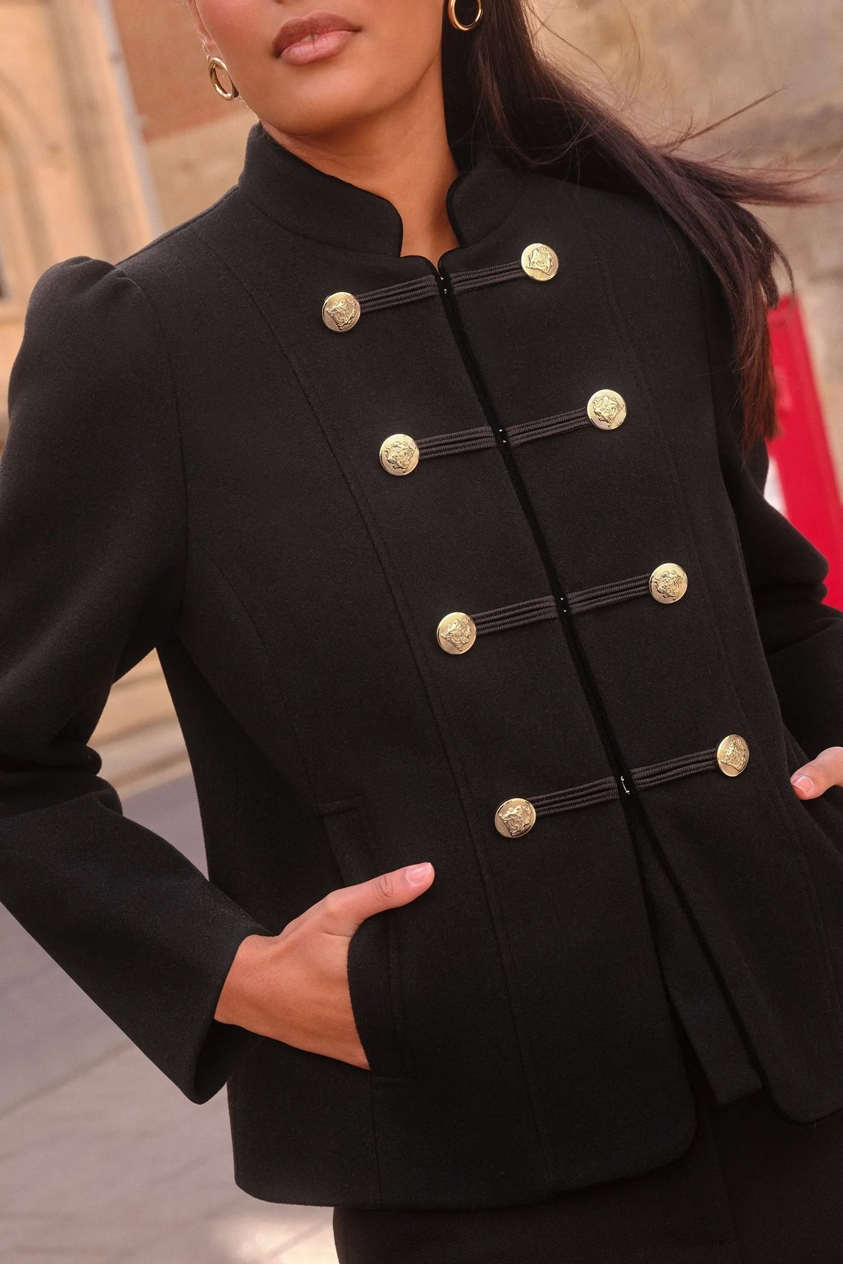 Detailaufnahme einer schwarzen Napoleon-Jacke mit goldenen Wappenknöpfen und schwarzen Zierschnüren am Stehkragen