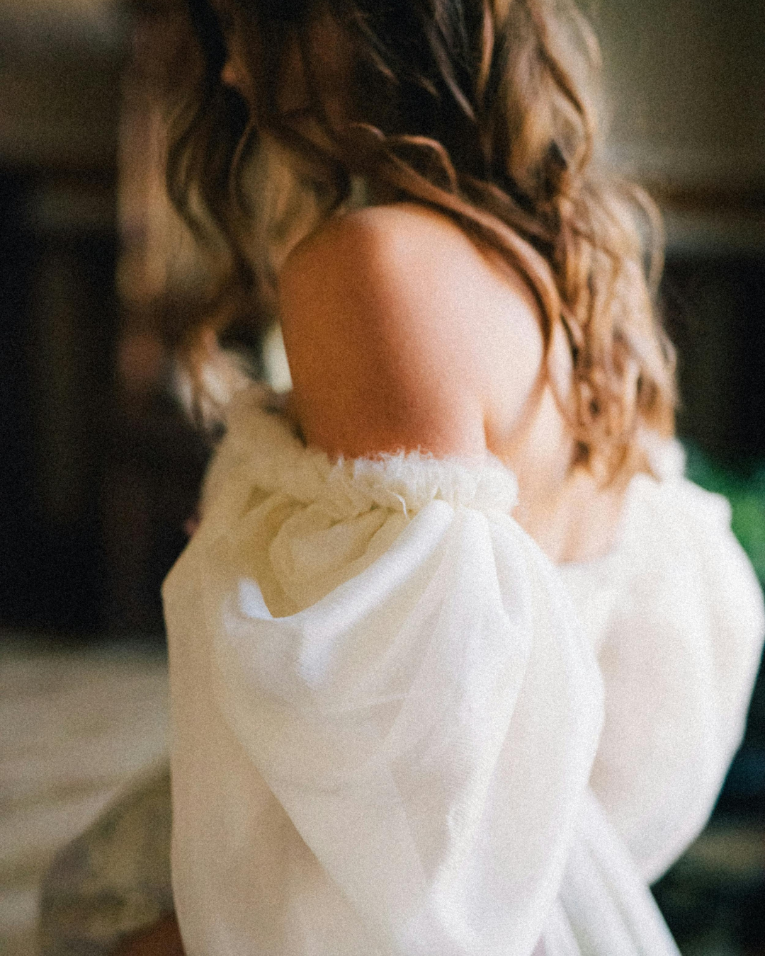 Nahaufnahme einer Frau mit schulterlangem, lockigem Haar, die ein weißes Kleid mit puffigem Ärmel trägt.