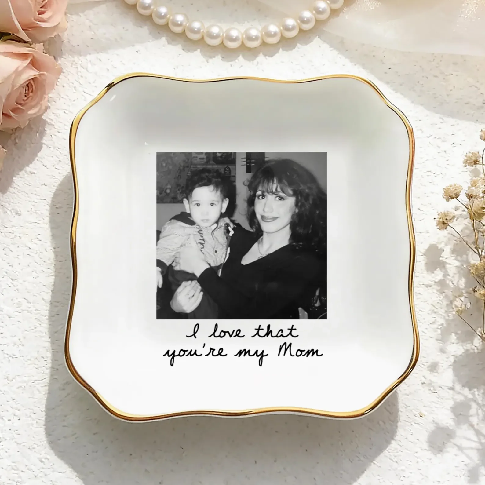 Quadratische, weiße Schmuckschale mit gewelltem Goldrand. In der Mitte ein gedrucktes Schwarz-Weiß-Foto von Mutter und Kind, darunter der Text „I love that you're my Mom“.