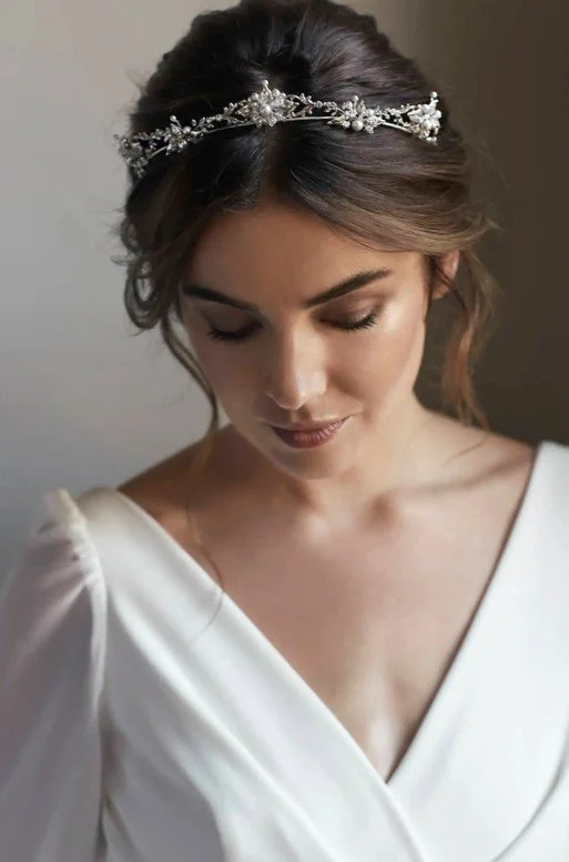 Elegante Braut mit hochgesteckten Haaren und einem filigranen, mit Perlen besetzten Diadem für die Hochzeit, den Blick sanft nach unten gerichtet.