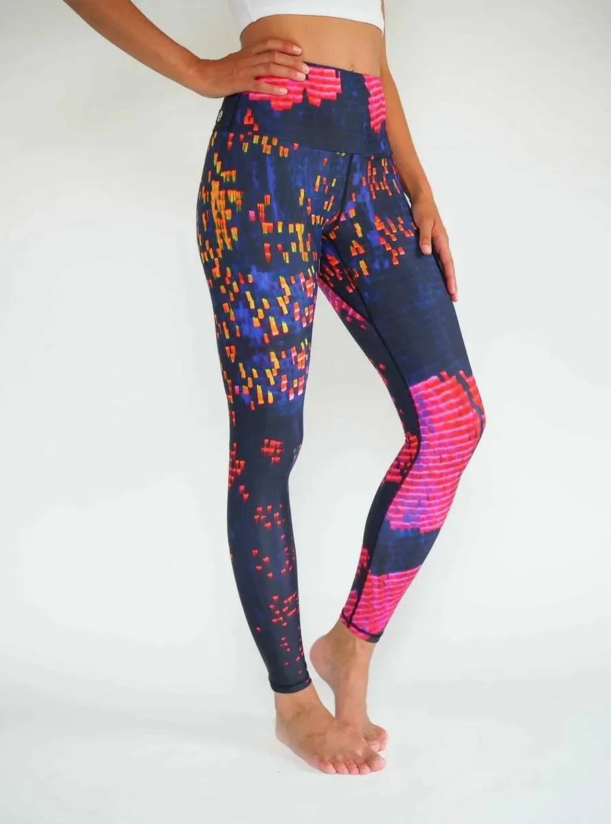 Frau in weißem Top und dunkelblauen Leggings mit abstraktem pink-orangem Muster vor hellem Hintergrund