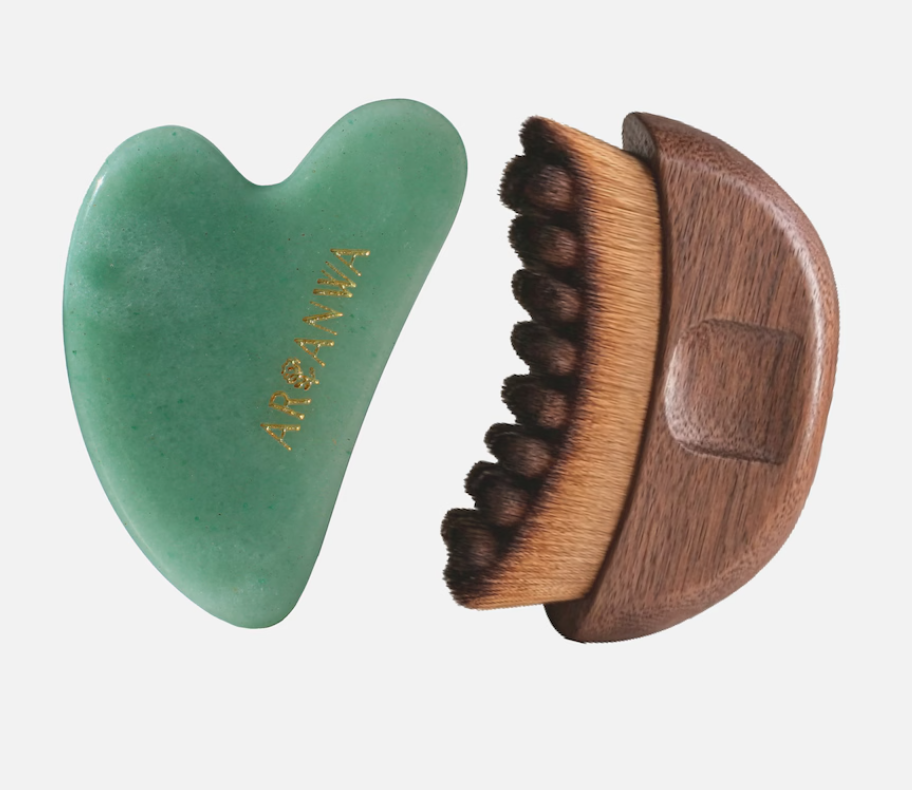 Herzförmiger Gua-Sha-Stein aus grüner Jade neben einem Lifting Brush mit dunklen Borsten und halbmondförmigem Holzgriff