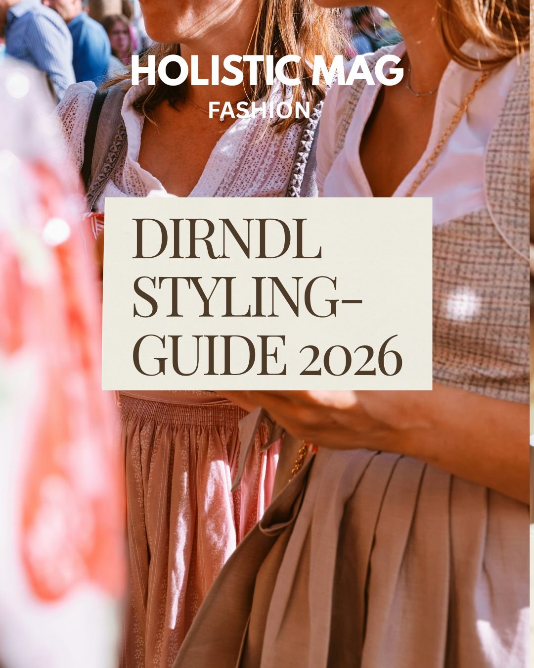 Zwei Frauen in Dirndln mit Spitzenbluse, Kropfkette und rosafarbenem bzw. beigem Rock stehen nah beieinander auf einem Volksfest, im Vordergrund verschwommene Menschenmenge und Deko; Textoverlay „HOLISTIC MAG FASHION – Dirndl Styling-Guide 2026".