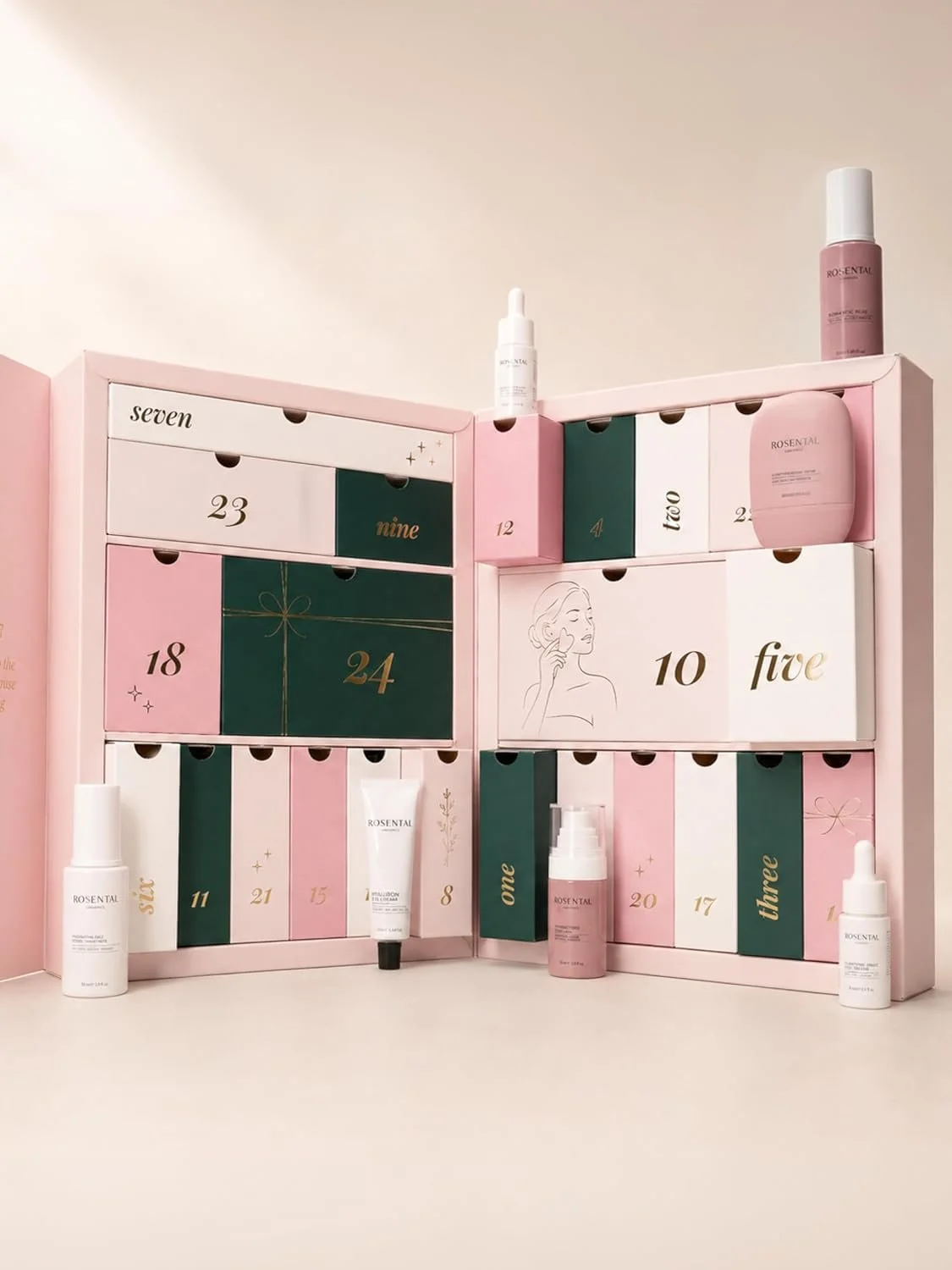 Ein geöffneter, zartrosafarbener Beauty-Adventskalender von Rosental mit unterschiedlich großen Schubladen in Rosa, Weiß und Dunkelgrün. Um den Kalender herum sind einige der enthaltenen Hautpflegeprodukte wie Seren und Cremes arrangiert.