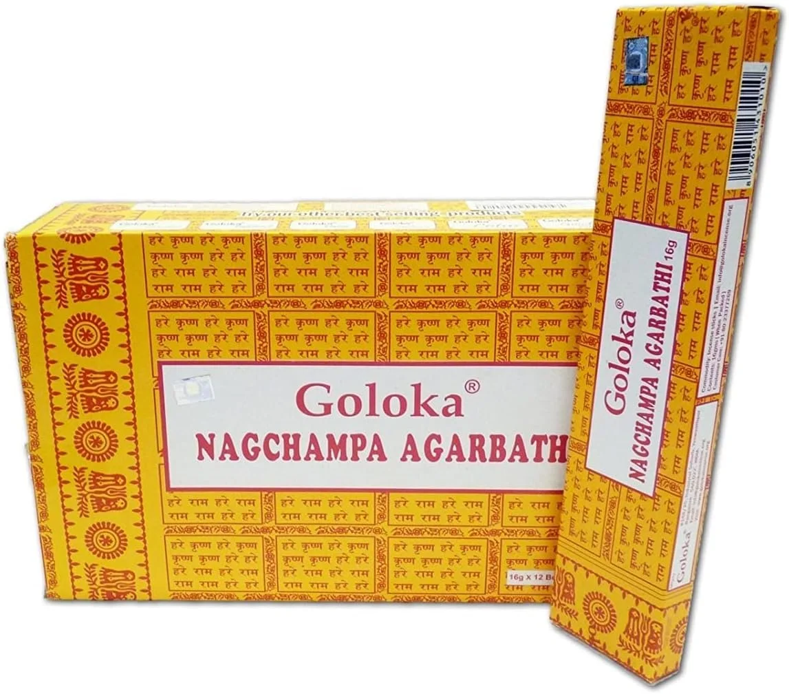 Eine große, gelbe Vorratsschachtel und eine darauf liegende Einzelpackung der Räucherstäbchen "Goloka Nagchampa Agarbathi". Beide Verpackungen sind auffällig mit roten Schriftzügen und einem Muster aus indischen Schriftzeichen bedruckt.