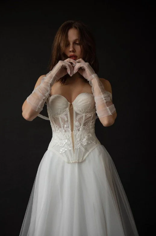 Detailaufnahme eines modernen Brautkleides mit halbtransparentem Korsett, floraler Spitzen-Verzierung und eleganten, gerafften Tüll-Handschuhen.