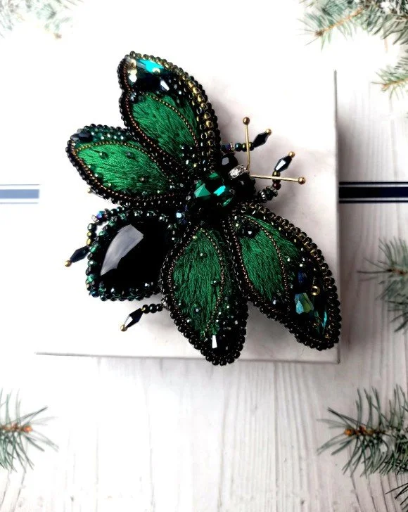 Eine filigrane Libellen-Brosche mit smaragdgrünen, transparenten Flügeln und einem silbernen, mit kleinen Kristallen besetzten Körper.