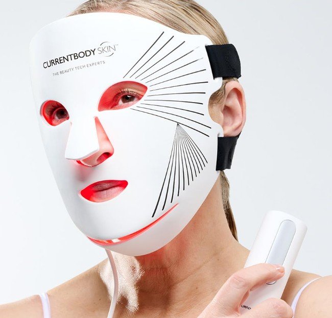 Flexible CurrentBody Skin LED-Lichttherapie Maske. Das Bild zeigt eine Frau bei der Anwendung der weichen Silikonmaske, die rotes Licht zur Anti-Aging-Behandlung ausstrahlt, inklusive Hand-Controller.
