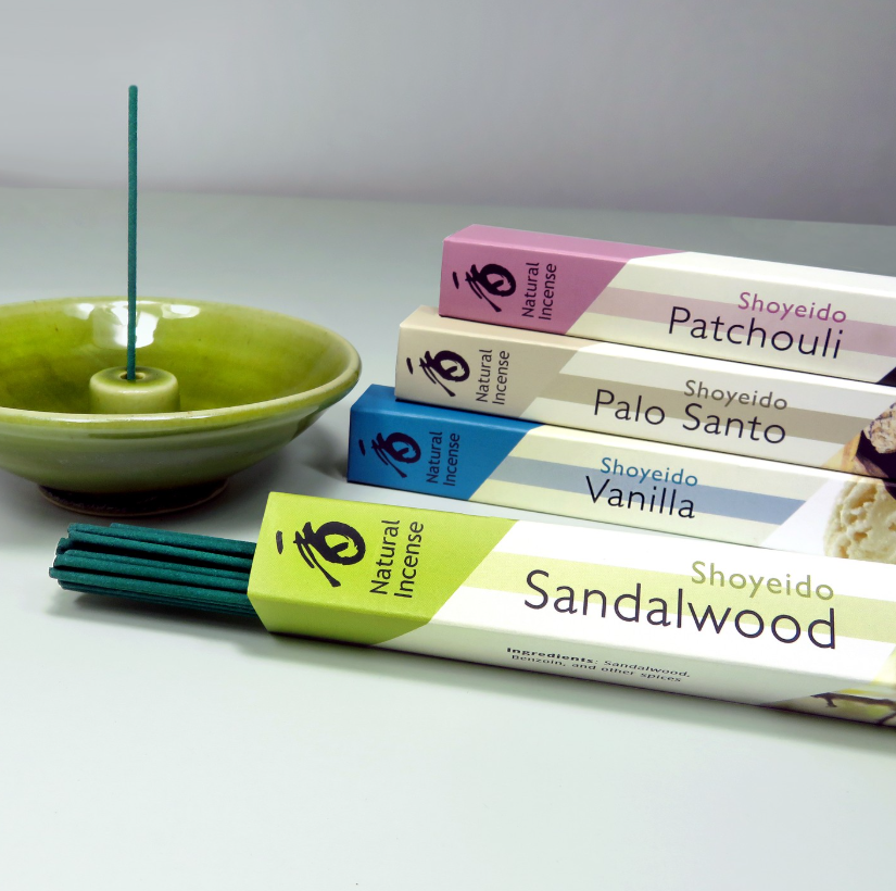 Shoyeido Räucherstäbchen aus Japan in den Duftrichtungen Patchouli, Palo Santo, Vanilla und Sandalwood, mit grünem Halter und brennendem Stäbchen.