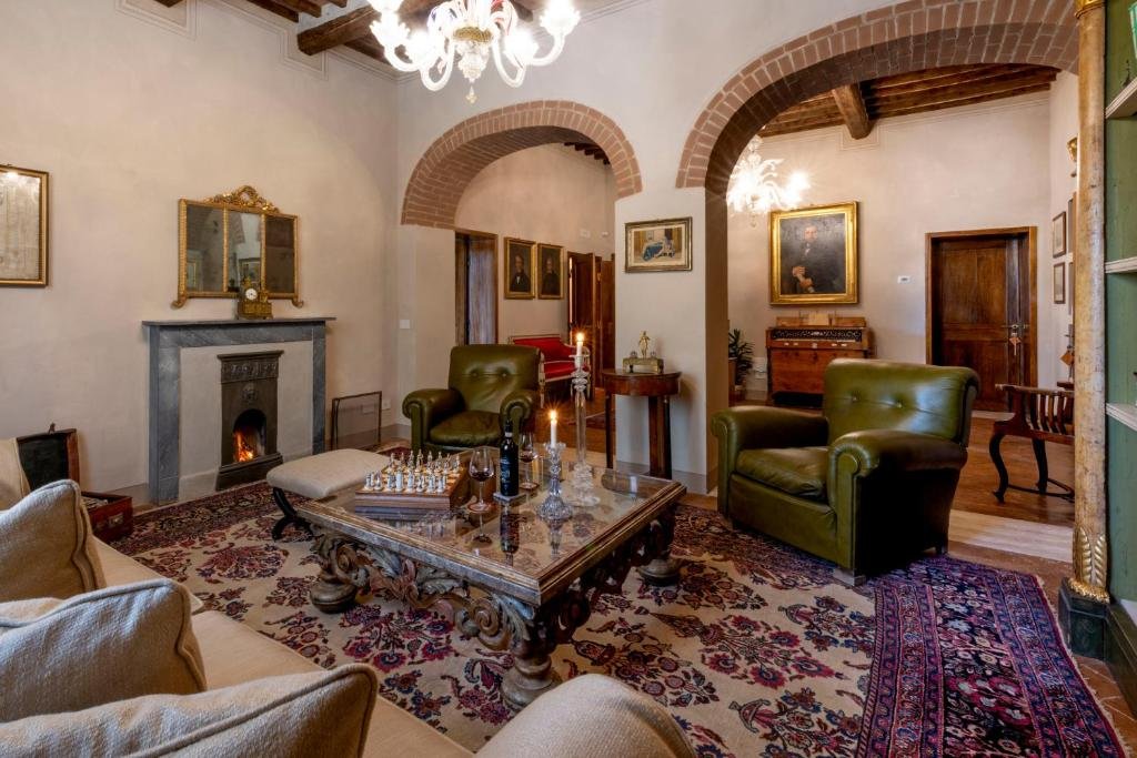 Foto eines eleganten Kaminzimmers mit grünen Ledersesseln, einem kunstvollen Couchtisch mit Schachbrett und antiken Teppichen unter gemauerten Rundbögen.