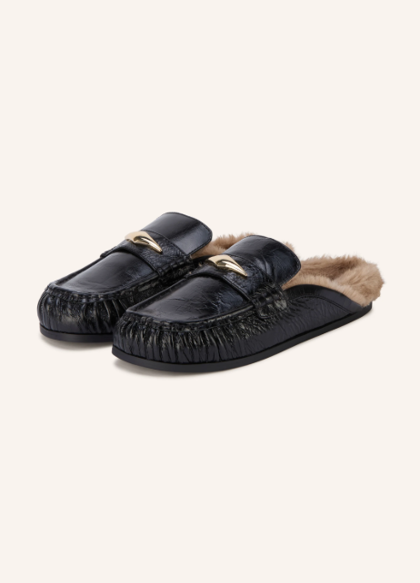 Schwarze Mules aus geprägtem Leder im Mokassin-Stil, verziert mit einer goldfarbenen Metallspange und hellbraunem Lammfell-Innenfutter